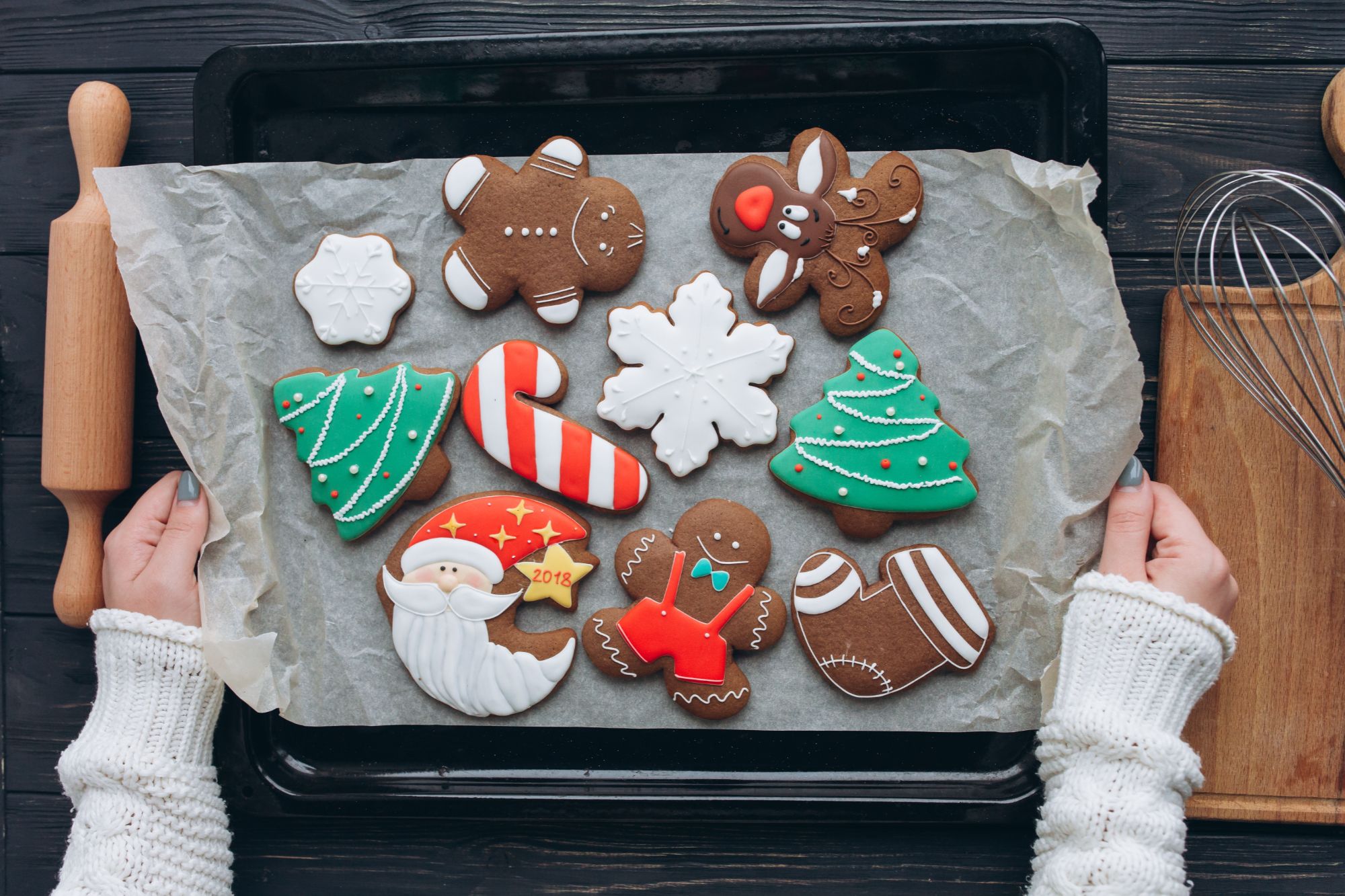 Hands decorating gingerbread house cookies at the holidays.
