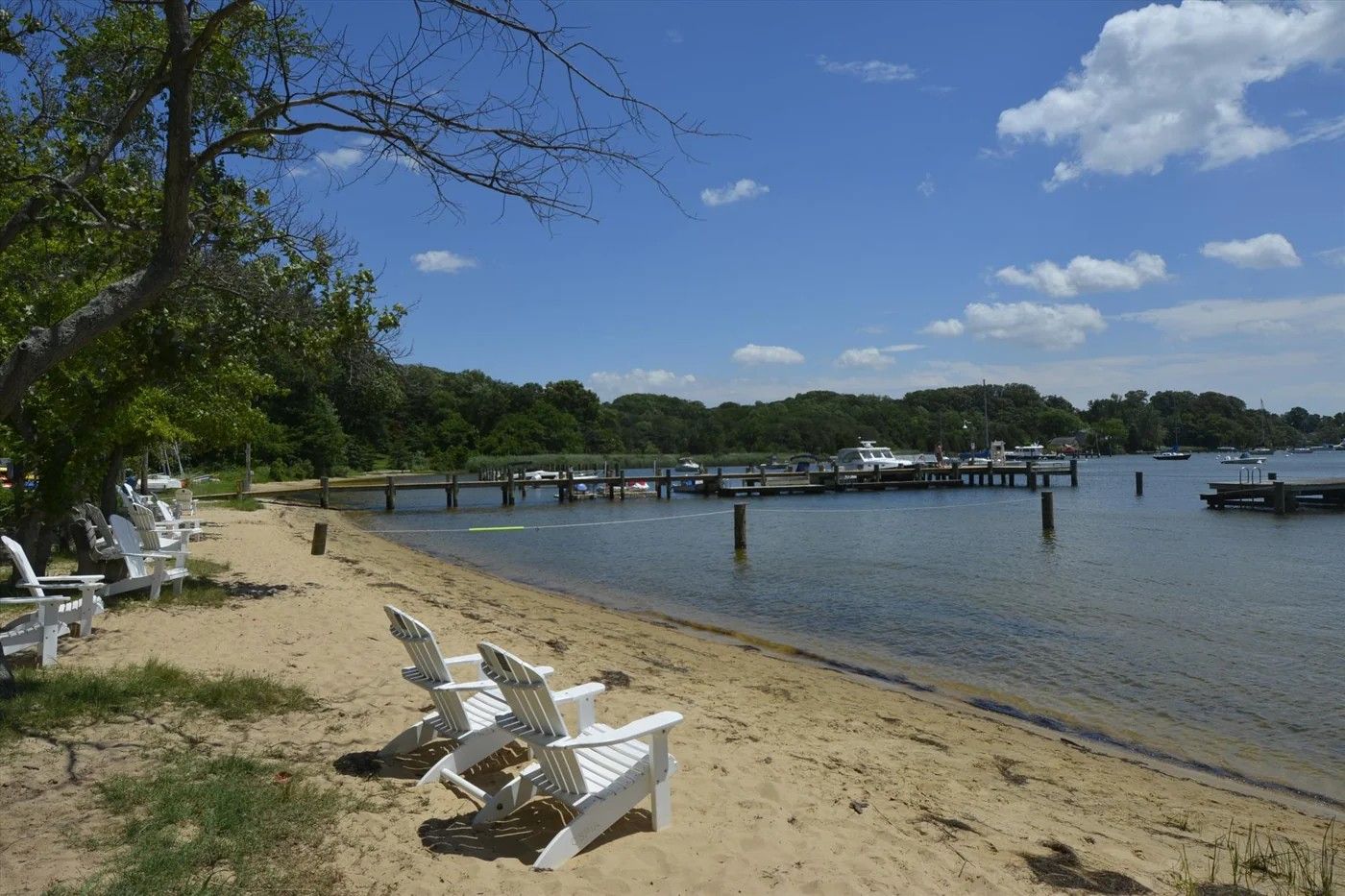 White Adirondack chairs on the sandy beach at Hatton Memorial Beach, with community piers on Sullivan's Cove beyond