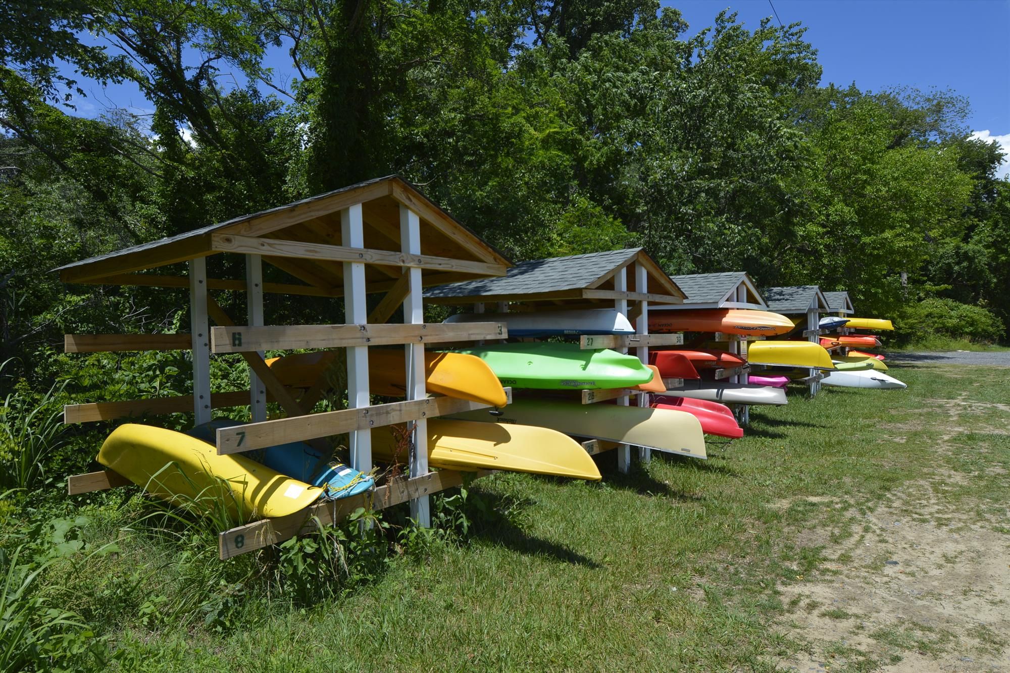 Covered wooden kayak racks holding brightly colored kayaks near the beach
