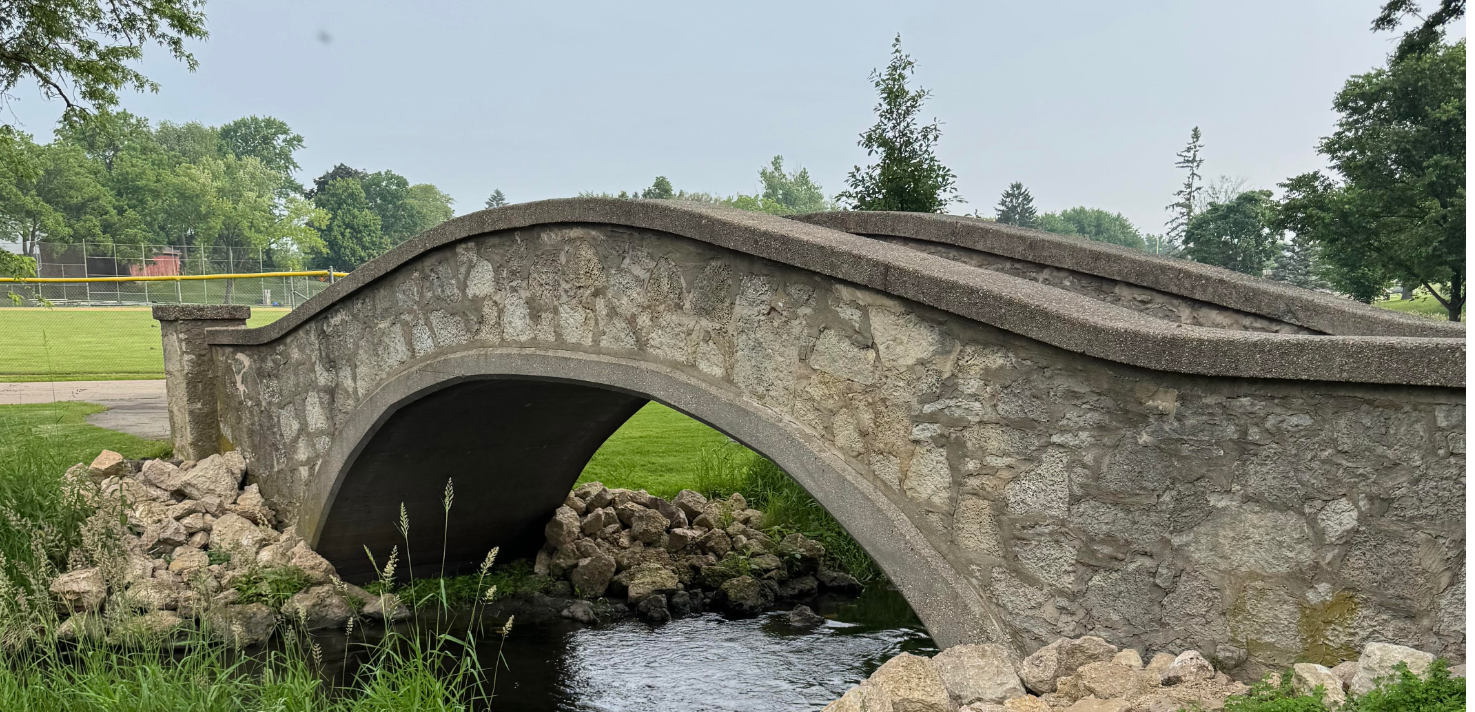 Stone pedestrian bridge over a creek at Village Park in Waunakee, Wisconsin, representing current buyer and seller market conditions.