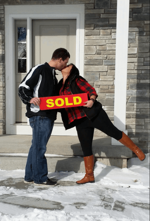 Couple celebrating an accepted offer with a SOLD sign in front of their new Wisconsin home