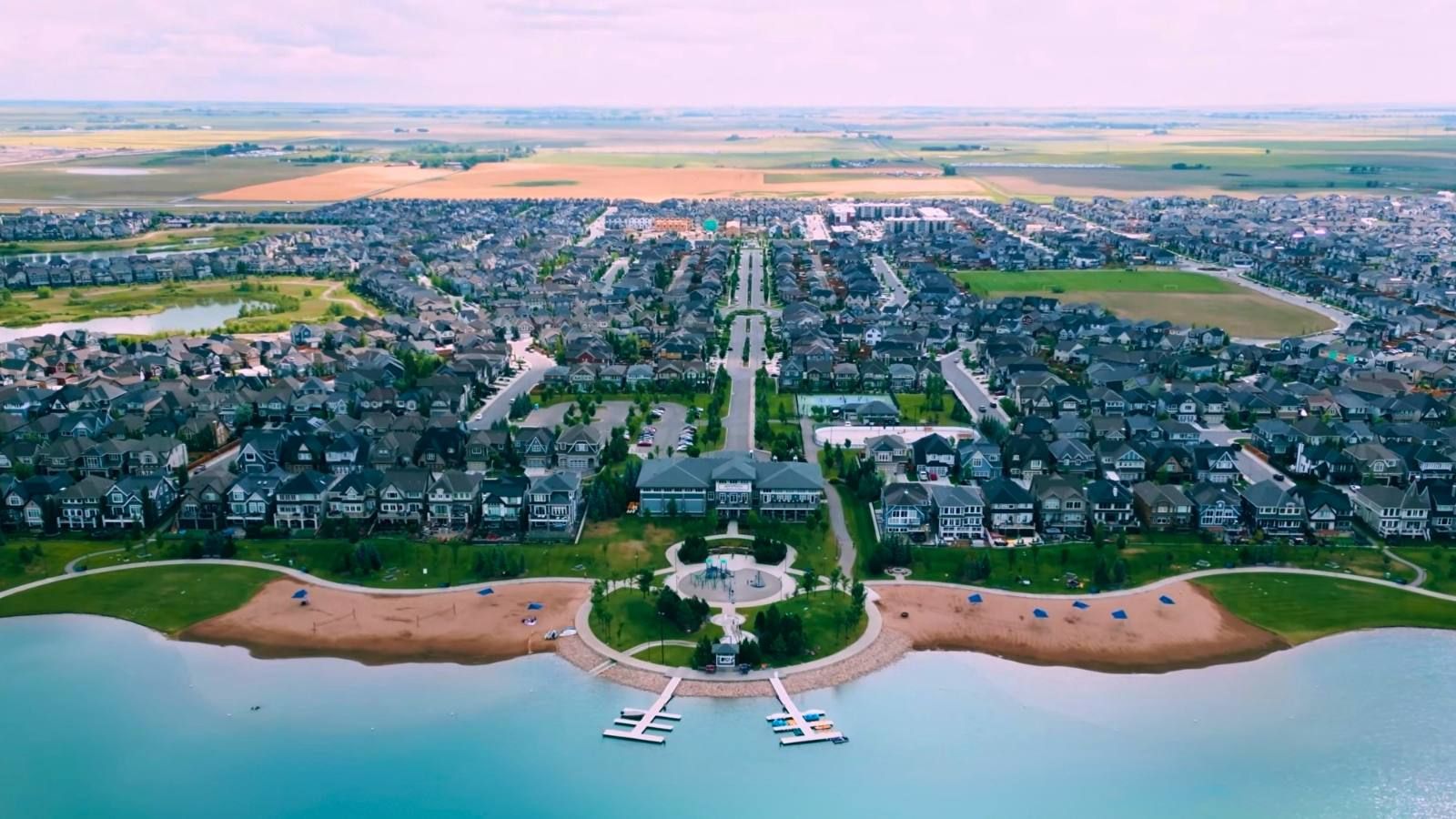 Aerial view of Mahogany Lake's main beach and Beach Club in Calgary, with twin sand beaches, floating docks and a boulevard running into the community