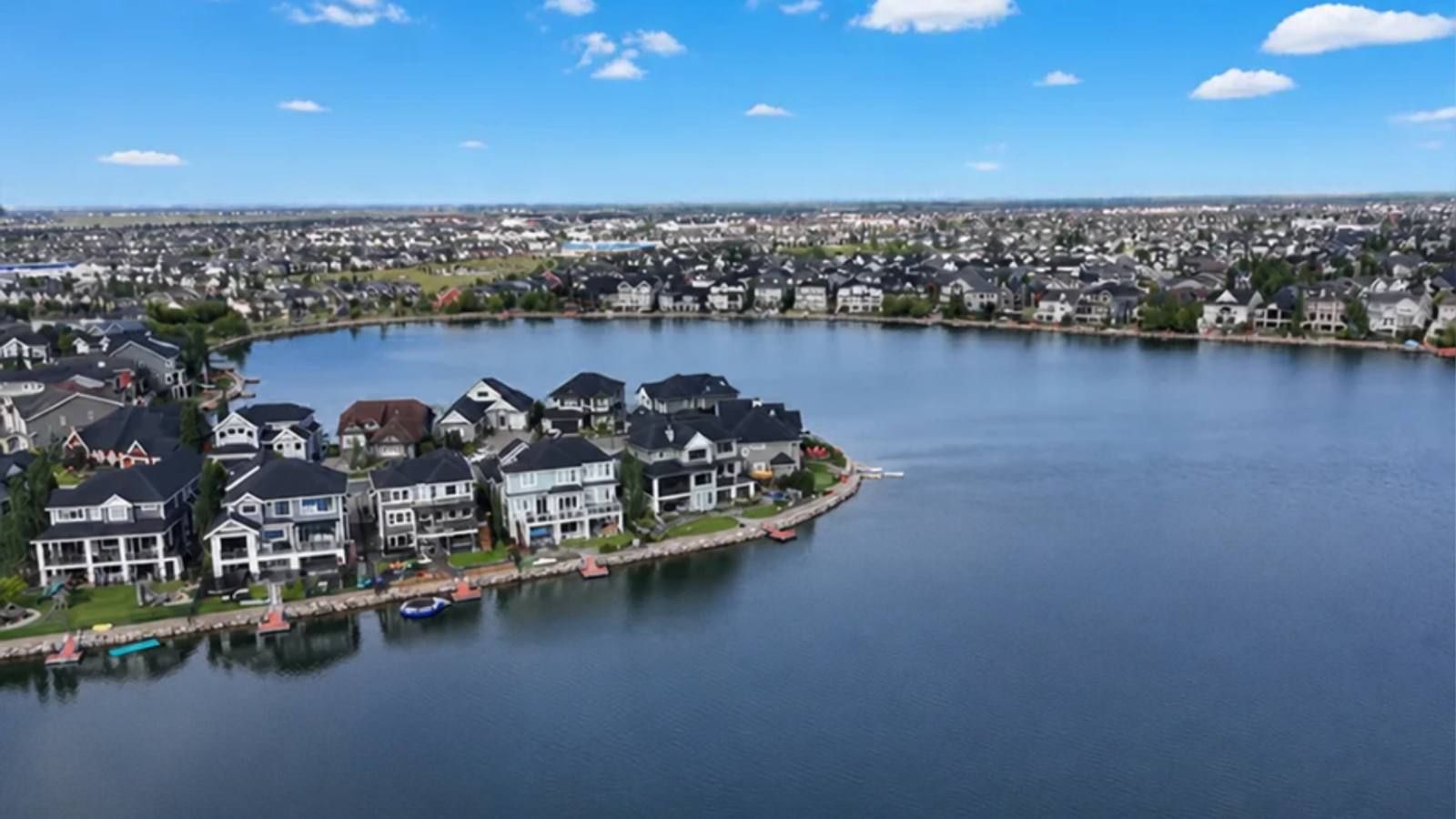 Aerial view of Auburn Bay Lake in Calgary, with a peninsula of lakefront homes with private docks and the community stretching along the far shore