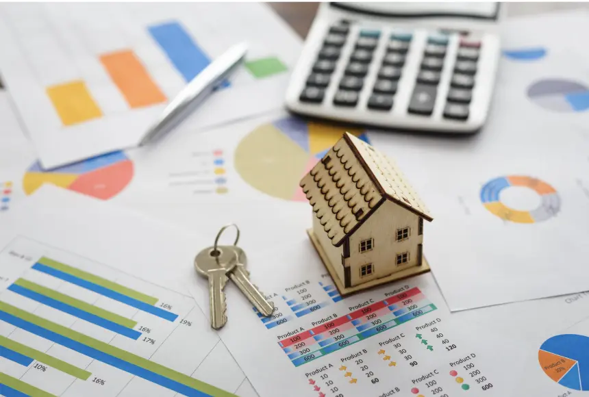 House key with miniature home on top of real estate market charts and financial graphs