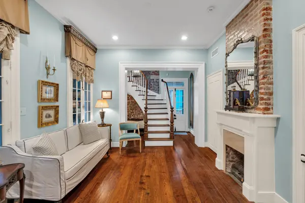 Staged blue parlor with exposed brick, fireplace and curved staircase in a historic New Orleans home