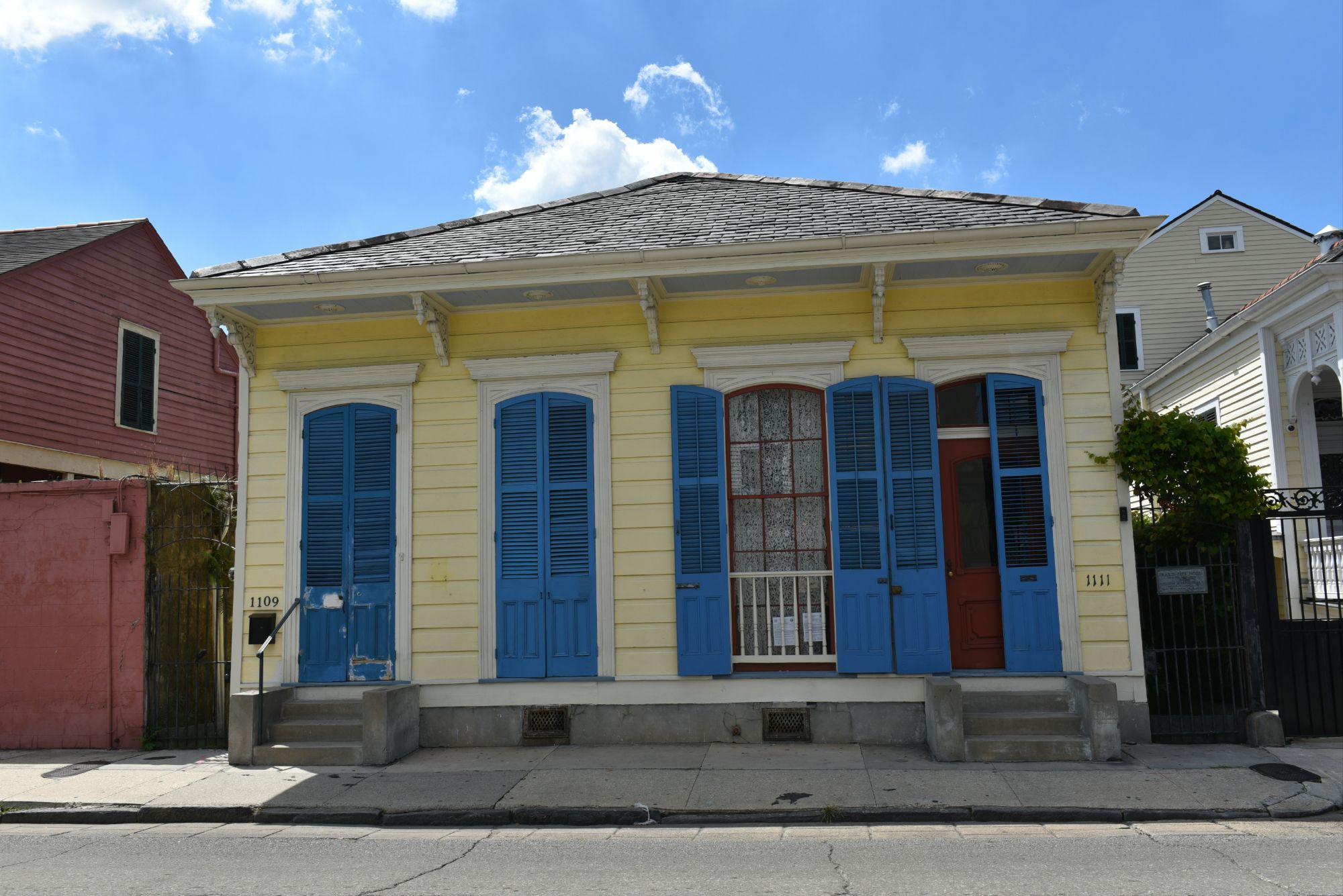 Pretty yellow shotgun house in NOLA with bright blue shutters. 