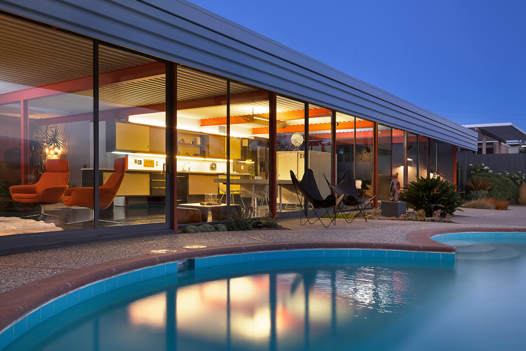 The Eichler X-100 at dusk, its glass rear wall lit up behind the pool