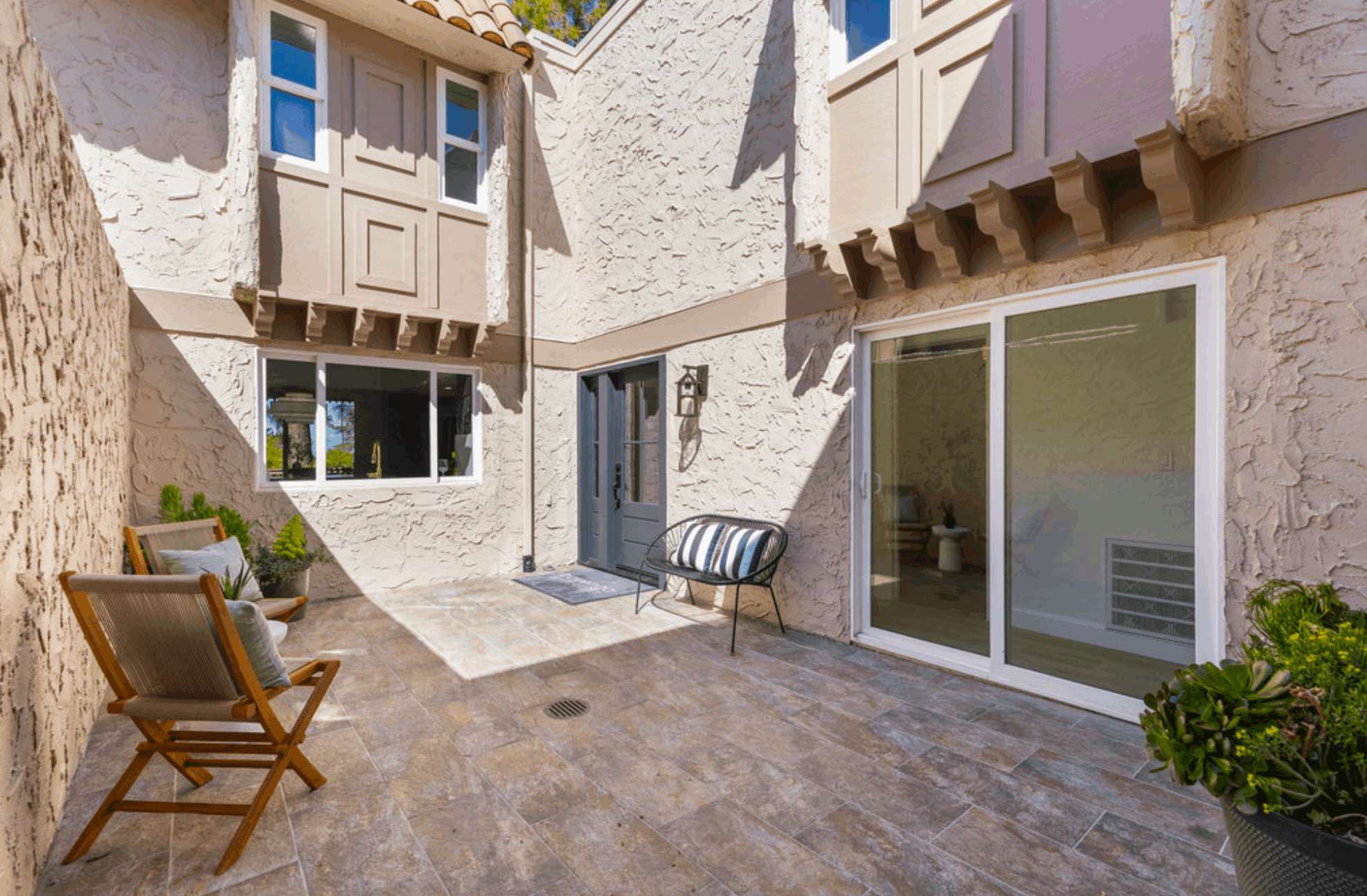 Brick-paved entry court with sliding glass doors and a wood balcony above