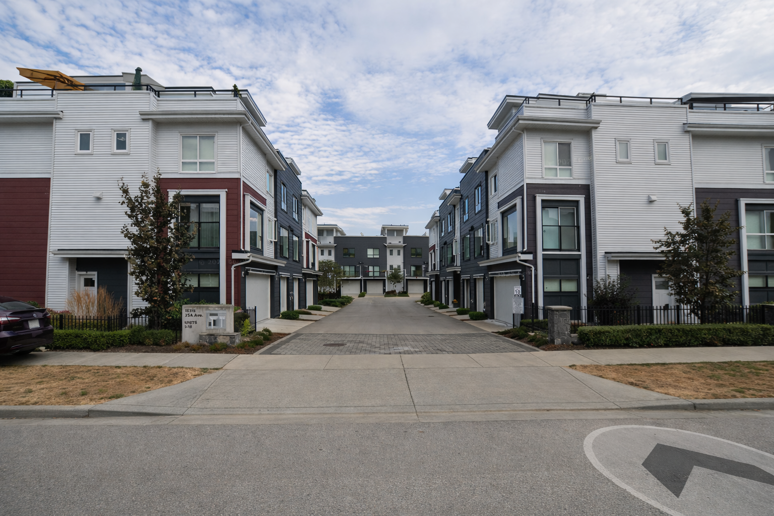 Street-level view of modern SOHO South Surrey townhomes at 16323 23 Ave, showing a clean residential roadway lined with three-storey units on both sides with garages and landscaped entrances.