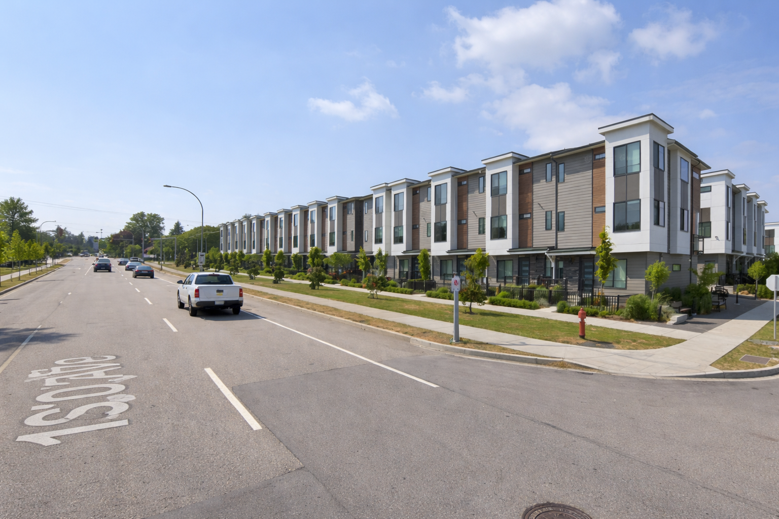 Wide street view of Horizon Townhomes along 162 Street in South Surrey showing modern 3-storey units, landscaped sidewalks, and roadway with passing traffic on a clear day