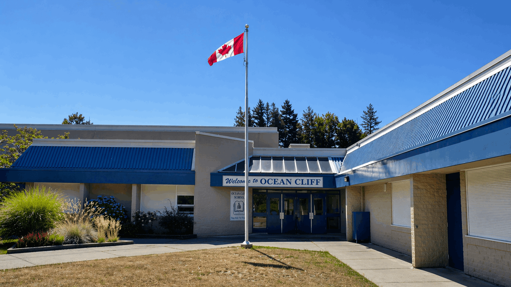 Front entrance of Ocean Cliff Elementary School in South Surrey with Canadian flag, blue awnings, and landscaped grounds on a clear day