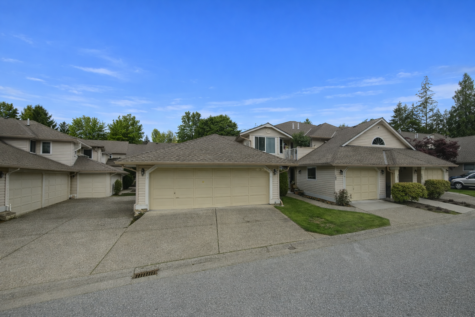 Street-level view inside Springfield townhome complex at 16031–16071 82 Avenue in Surrey, BC, showing roadway, parked vehicles, and two-storey beige townhomes from a standing perspective on the road