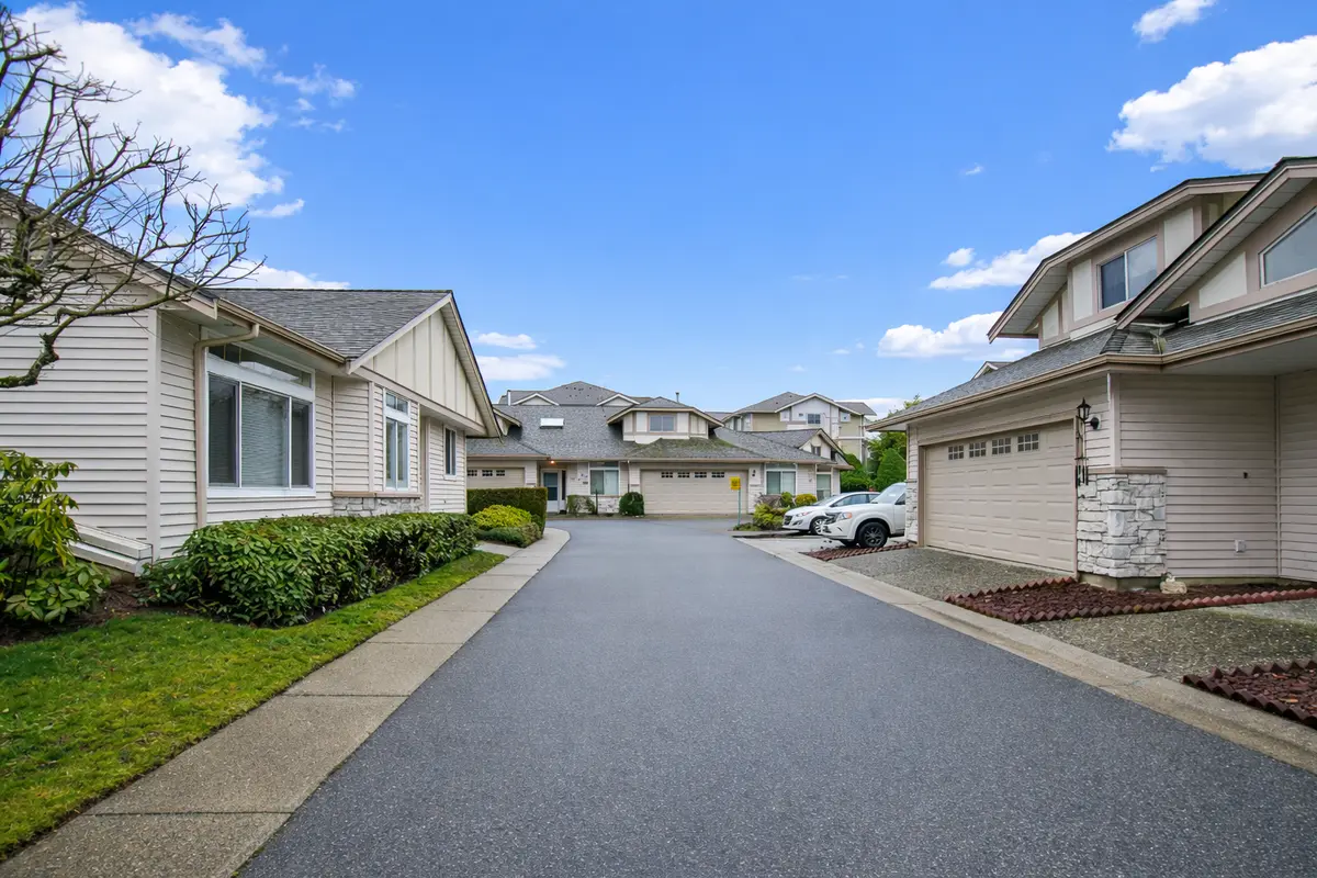 Street-level view inside Hampton Woods townhouse complex in Fleetwood Surrey, showing clean roadway, rancher-style homes, and landscaped surroundings under a clear blue sky