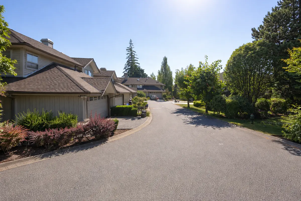 Interior street view of Oak Tree townhouse complex at 15860 82 Avenue in Fleetwood Surrey, showing landscaped roadway, mature greenery, and well-maintained homes under clear blue skies