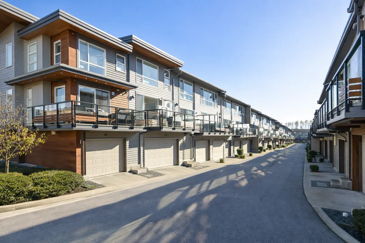 Street-level view of Breeze Townhomes by Adera in South Surrey, featuring modern West Coast architecture, garage-front units, glass railings, and a clean internal roadway.
