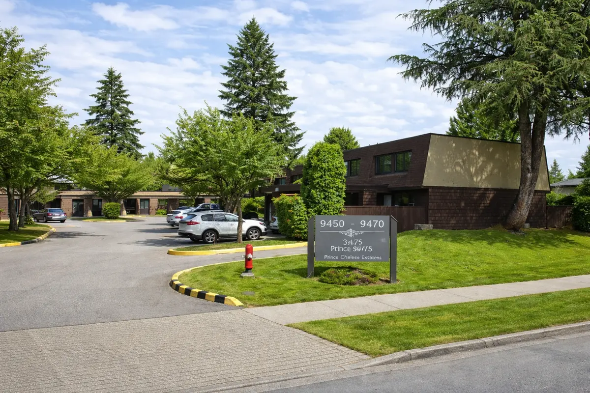 Street-level view of Prince Charles Estates townhouse entrance at 9450–9470 Prince Charles Boulevard in Surrey BC with green lawn, sign, and surrounding townhomes