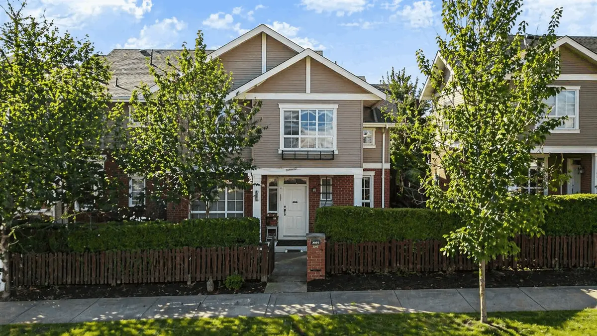Front exterior of Clayton Rise townhomes in Surrey BC featuring landscaped yard, leafy trees, fenced entry, and modern townhouse architecture in Clayton Heights.