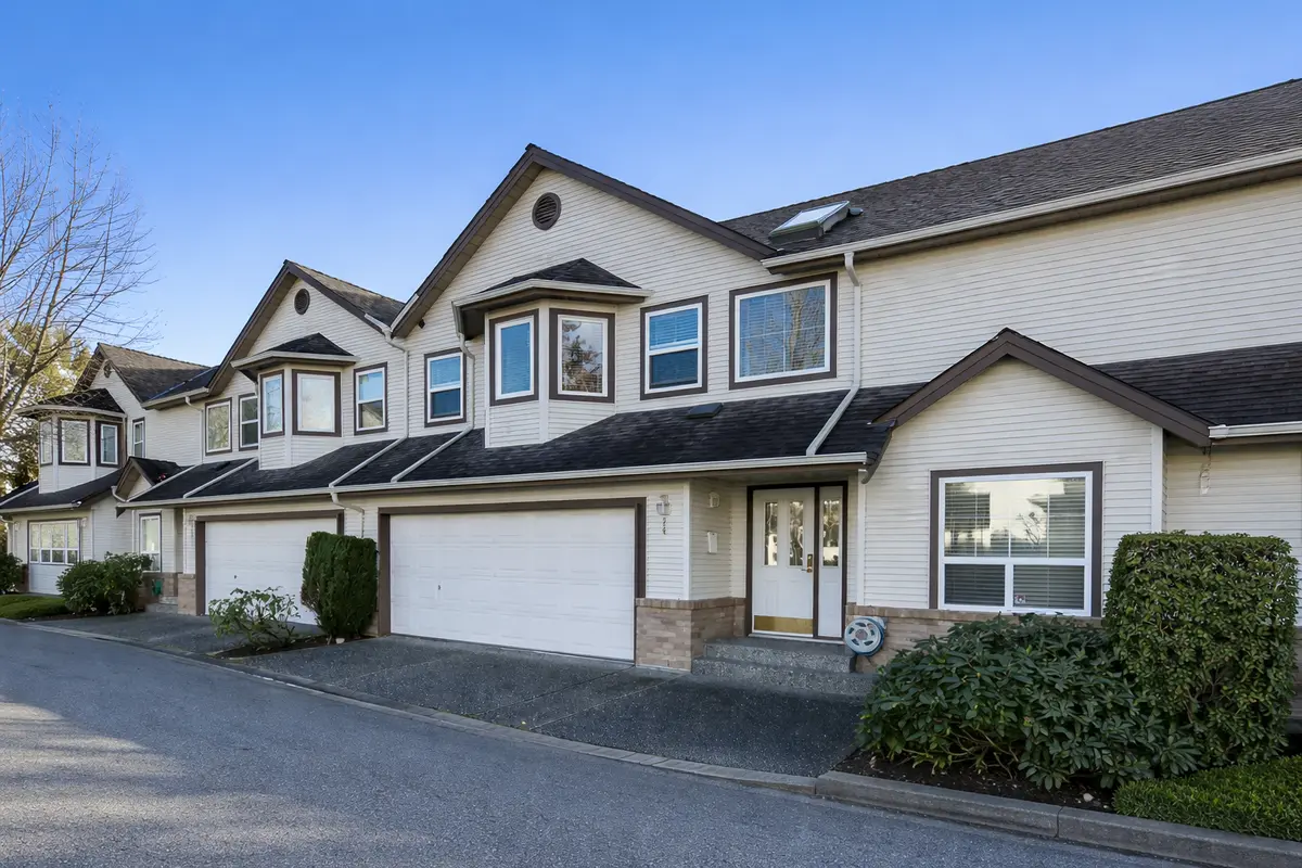Exterior view of Fleetwood Oaks townhomes in Surrey BC showing row of two-storey units with garages, landscaped frontage, and clear blue sky