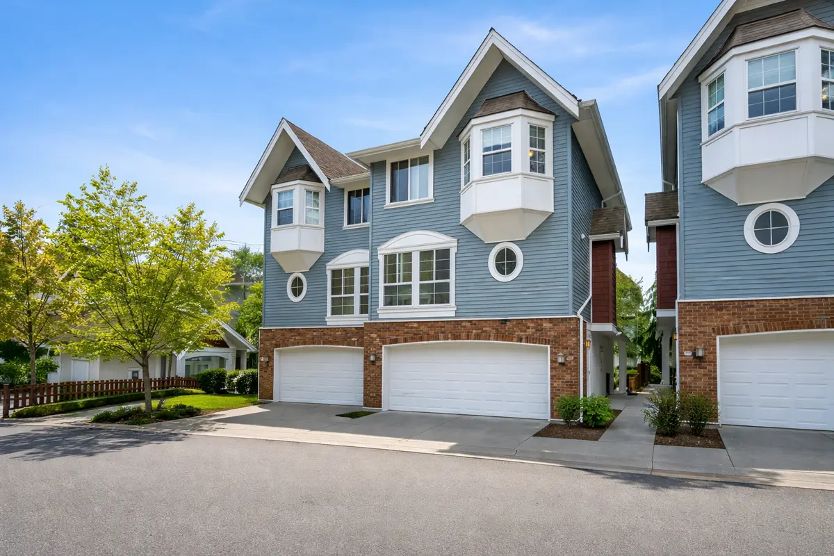 Street-level view of Sullivan Gardens townhomes at 5889 152 Street in Surrey BC showing three-storey units with garages, blue sky, and clean landscaping from the road