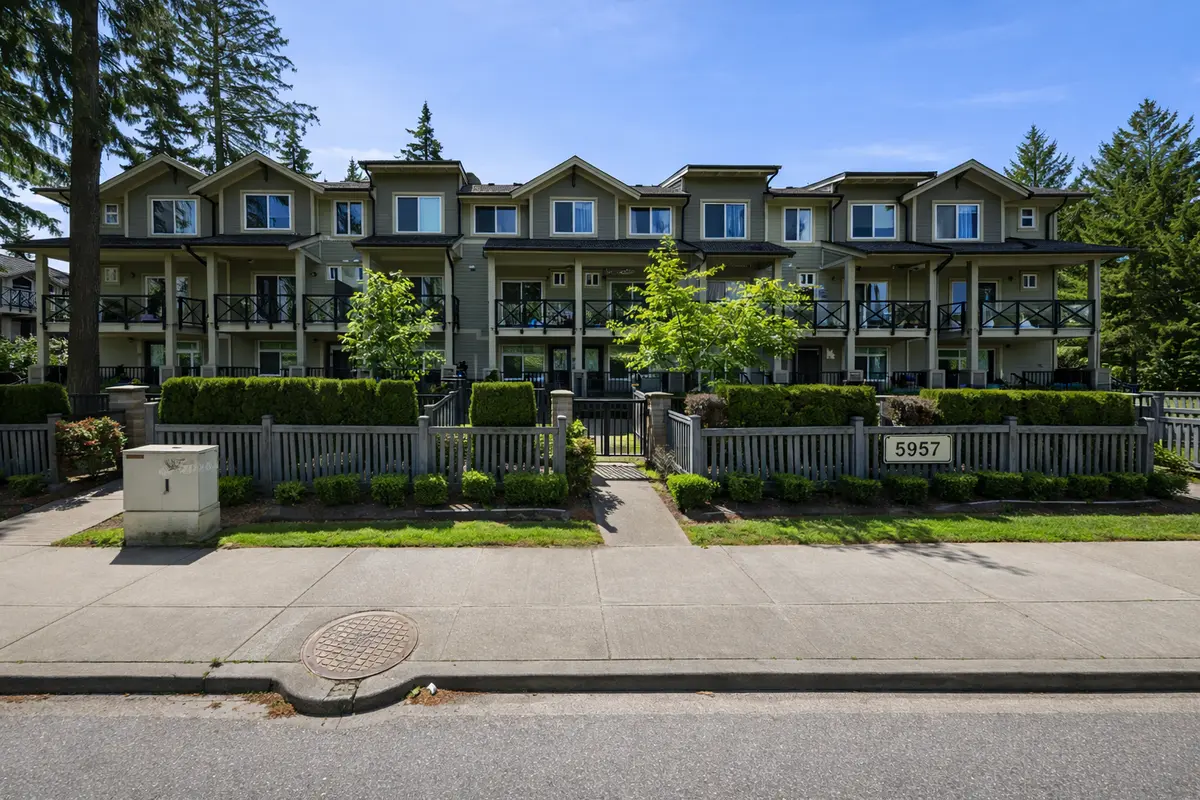 Sidewalk-level view of Panorama Station townhomes at 5957 152 Street in Surrey BC showing three-storey units, landscaped frontage, and clean exterior with reduced glare and clear visibility
