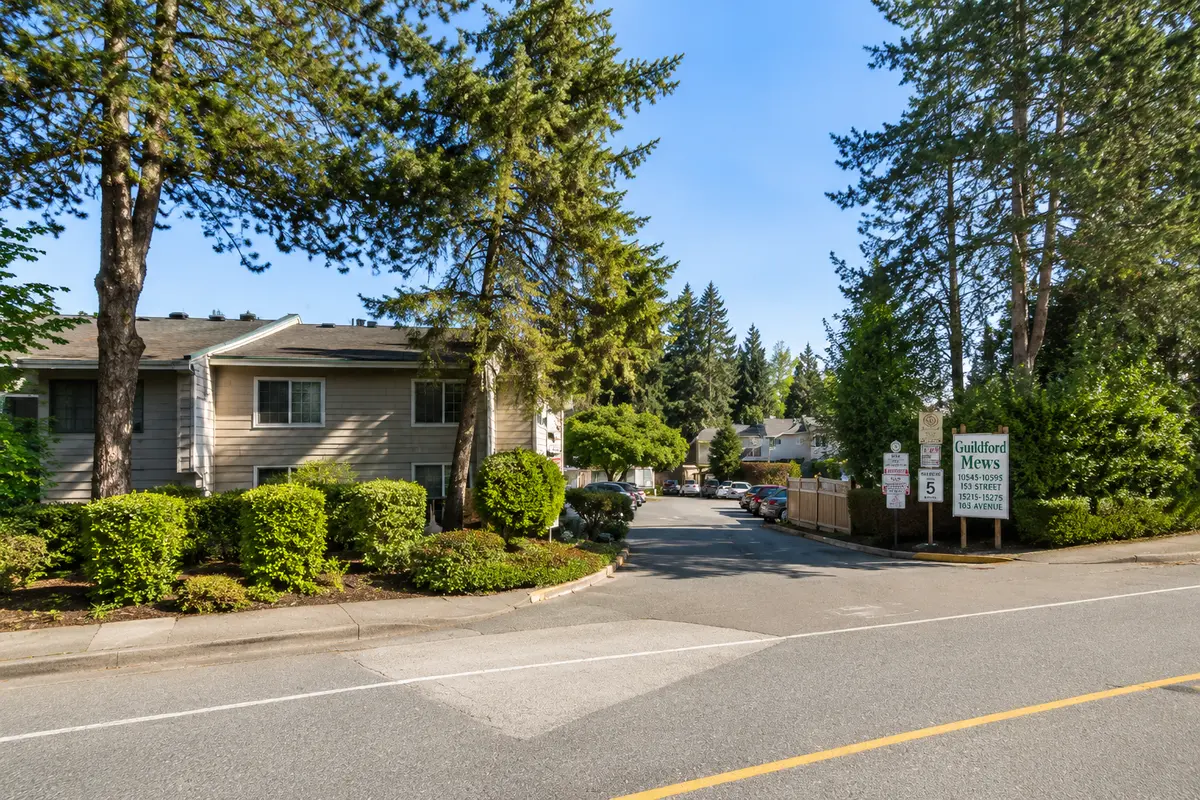 Street entrance to Guildford Mews townhomes at 10595 153 Street in Surrey BC with mature trees, landscaping, and townhouse community entrance signage