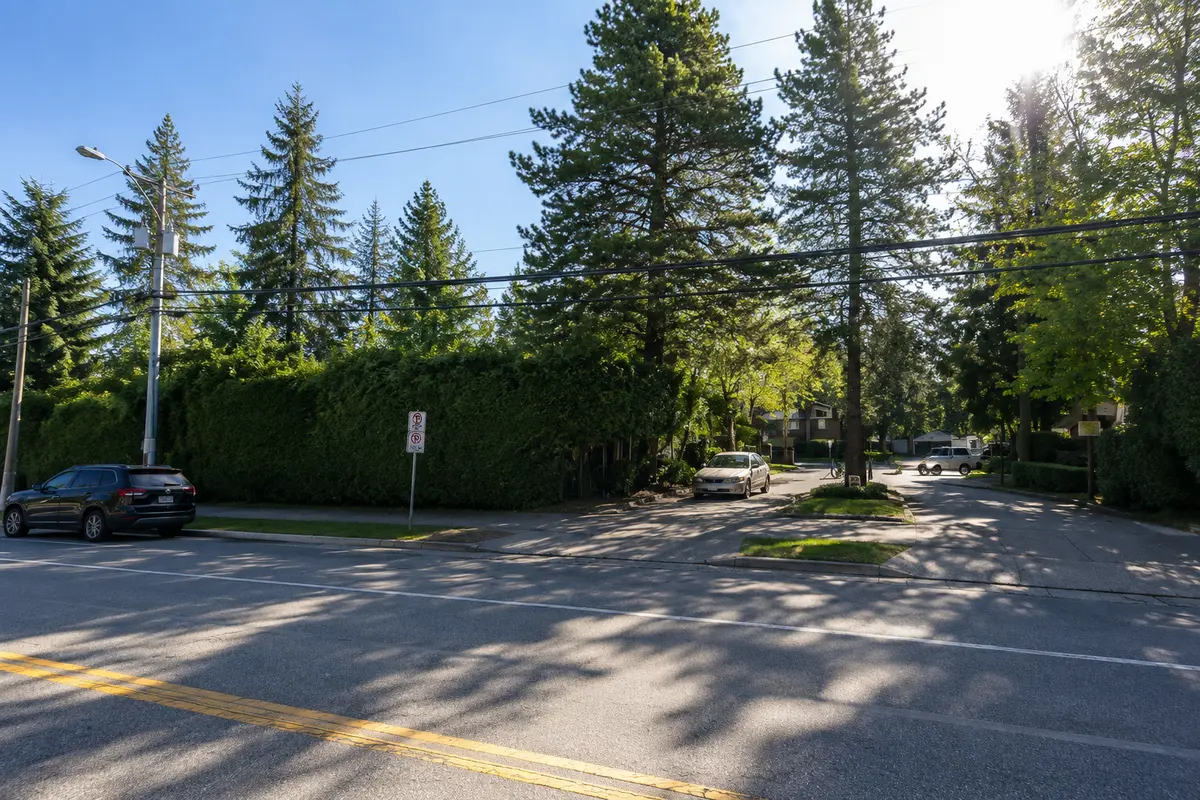 Main entrance to Lincoln's Gate townhouse community at 10620 150 Street in Guildford, Surrey BC, featuring mature evergreen trees, landscaped hedges, the entrance driveway, and a welcoming streetscape on a bright sunny day.