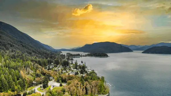 Lakefront homes along a forested north shore with a public dock and the lake stretching west