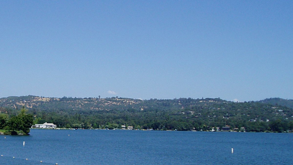 Homes among oaks and pines along the shoreline of Lake Wildwood near Penn Valley, California, under a clear blue sky