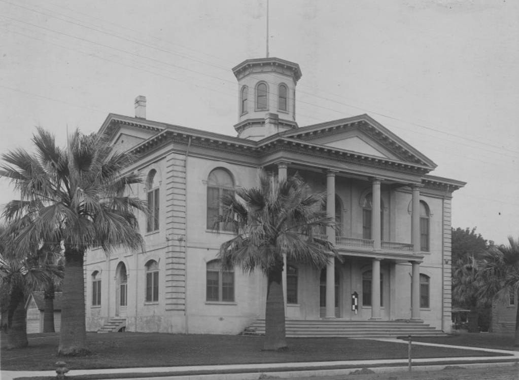 Black-and-white photo from about 1915 of the two-story Sutter County Courthouse in Yuba City, with columns, a domed cupola and tall palm trees on the front lawn