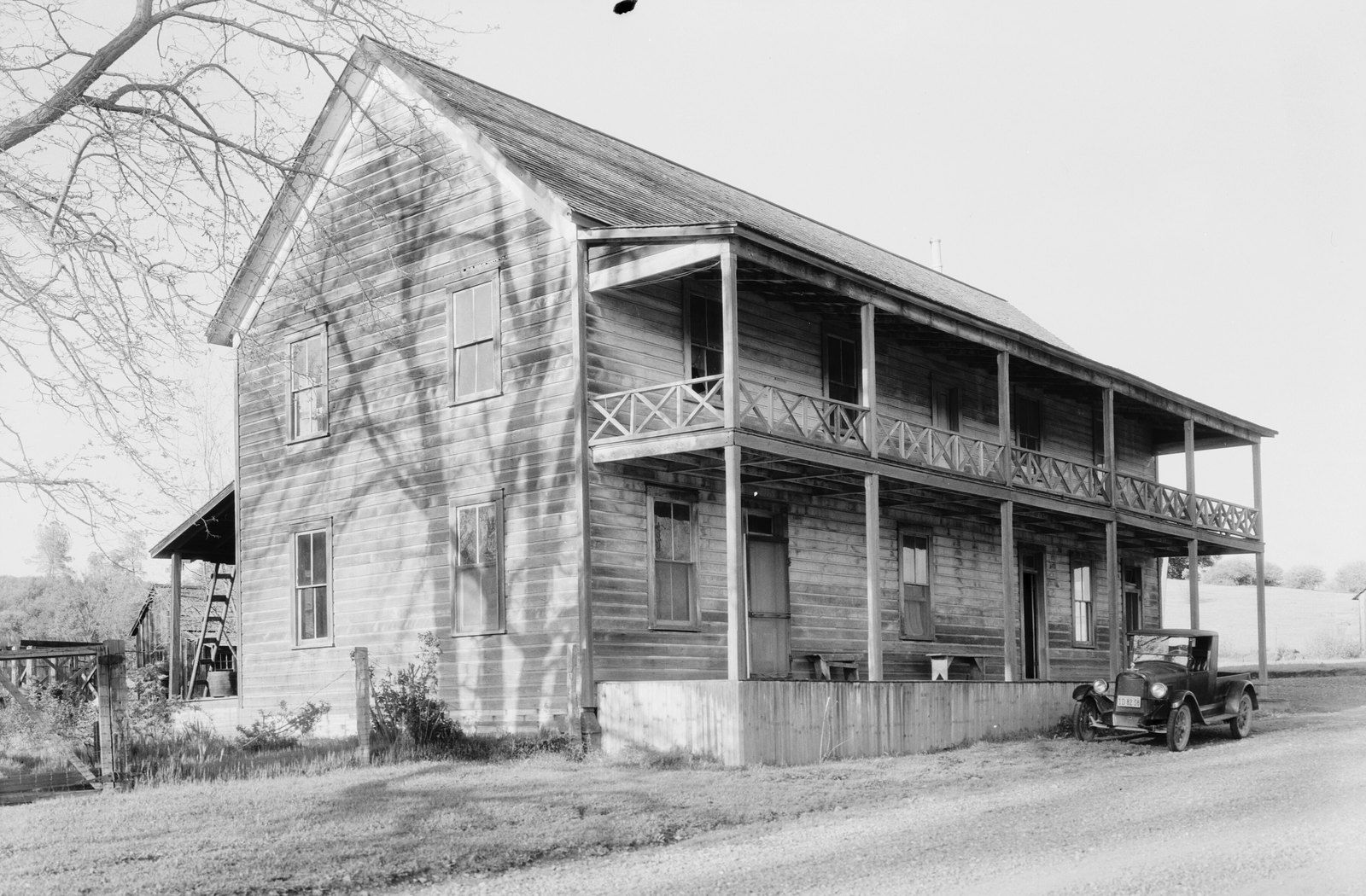 Black-and-white 1934 photo of the two-story wooden Oregon House roadhouse in the Yuba County foothills, with a long upper balcony, bare oak branches and a 1920s car parked on a gravel road