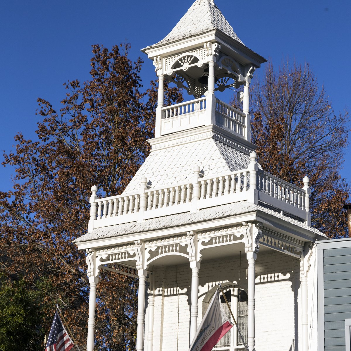 White Victorian Nevada City Firehouse No. 1 with a bell tower and ornate balconies on Main Street, framed by autumn trees and a deep blue sky