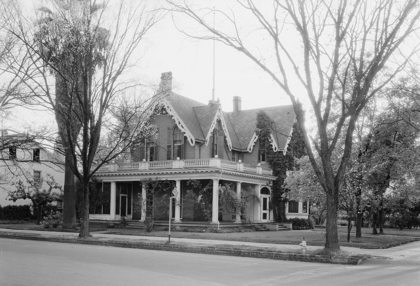 Black-and-white photo of a two-story Victorian home with a wraparound columned porch, steep gables and decorative trim on a tree-lined Marysville street corner
