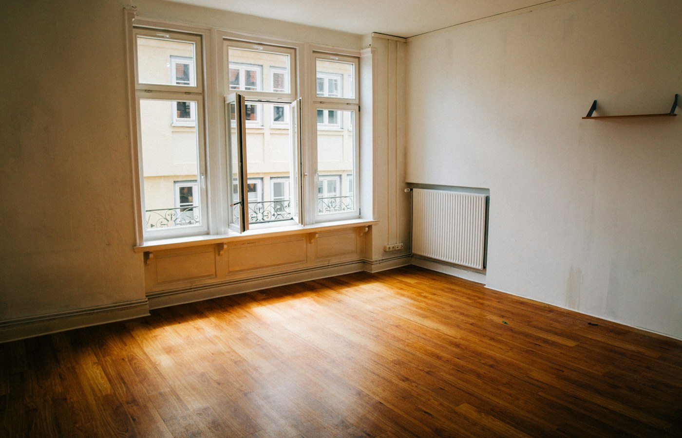 An empty room with wooden floors and tall windows, ready for a move