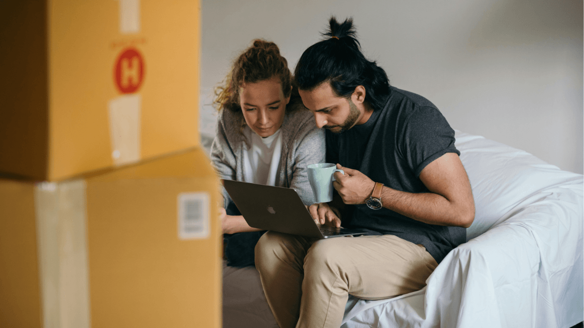 Couple using a laptop while surrounded by moving boxes, illustrating how homeowners can coordinate buying a new home and selling their current home at the same time