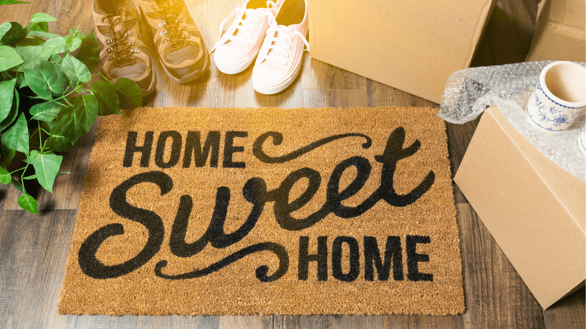 Home Sweet Home doormat with moving boxes and shoes, representing the emotional connection, lifestyle goals and sense of belonging that motivate home buyers to make offers in the North Dallas real estate market