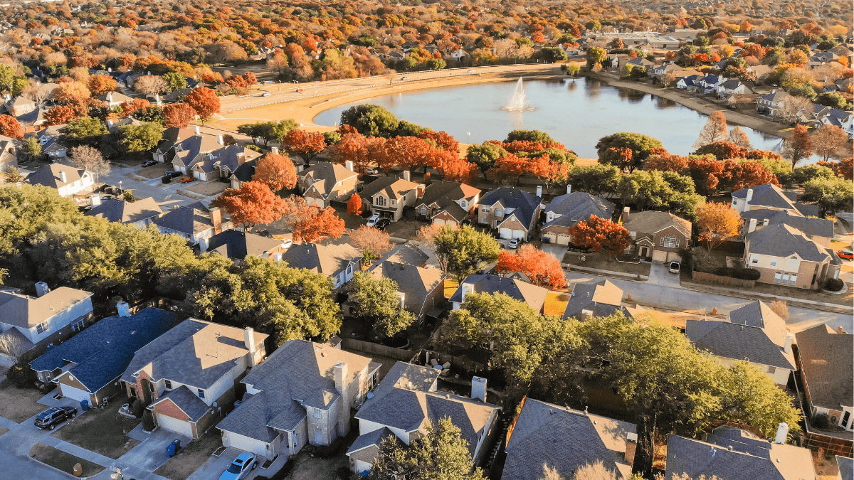 Aerial view of a tree-lined Dallas-area neighborhood with a community lake and fall foliage, representing popular neighborhoods in North Dallas, Richardson, Plano, Allen and Lake Highlands attracting today’s home buyers