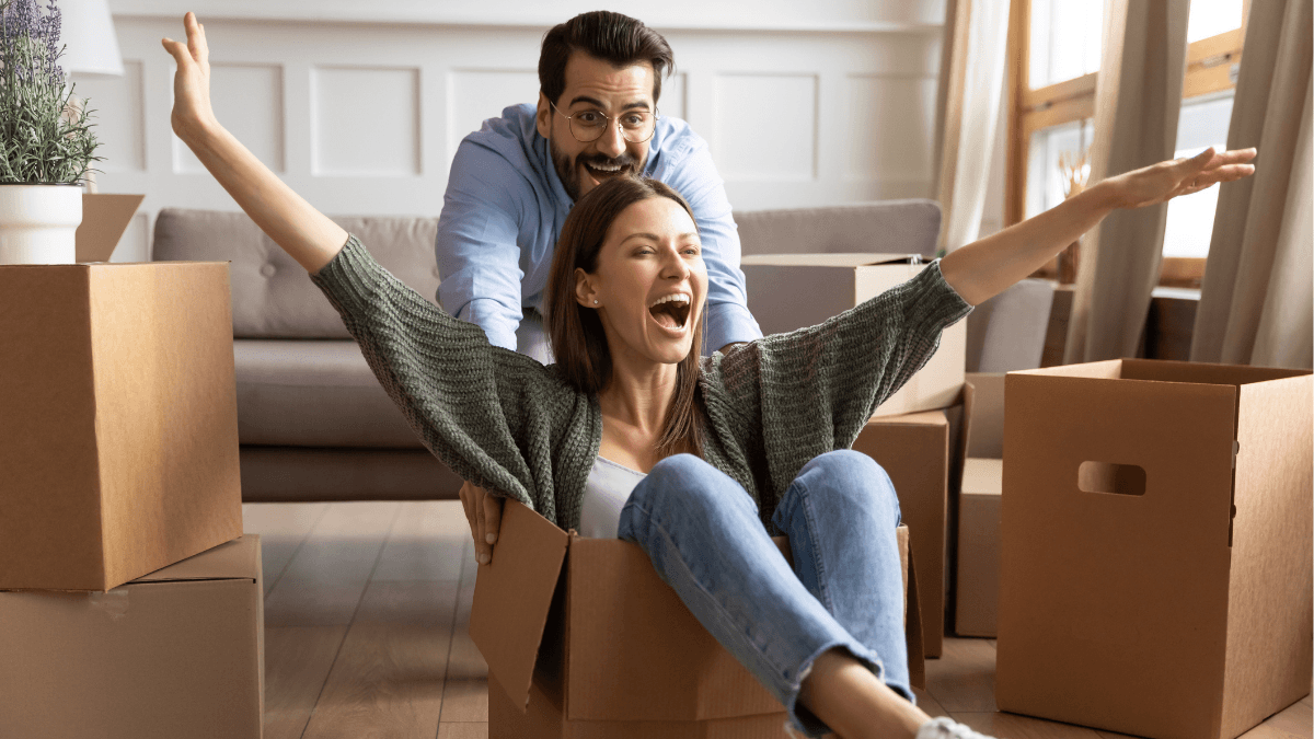 Happy home buyers surrounded by moving boxes, representing how buyers emotionally picture themselves living in a home during a showing and what influences their impressions, confidence and decision to make an offer