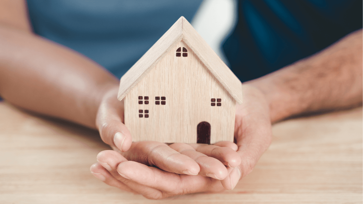 Wooden model home held carefully in two hands, representing smart pricing, preparation and marketing strategies that help Dallas-area homeowners sell quickly without sacrificing home value