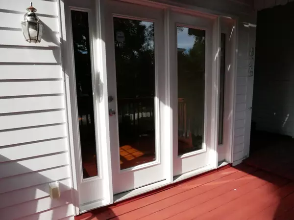 Back deck with white French doors, white siding, red painted wooden deck, and a wall-mounted outdoor light fixture.