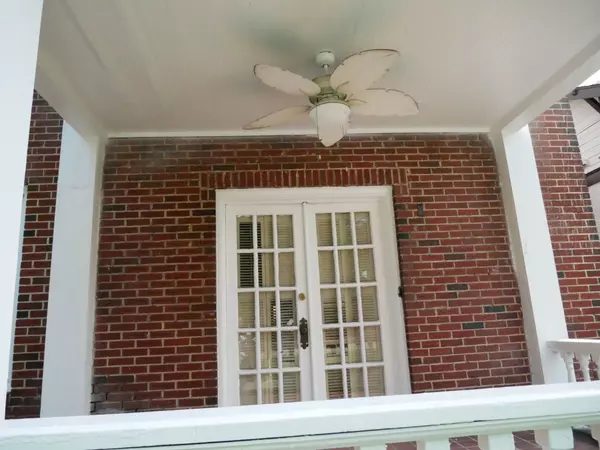 Front porch view showing French doors with glass panes, brick wall, and a ceiling fan with leaf-shaped blades.