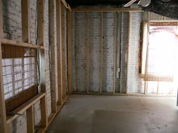 Unfinished basement room with white painted brick walls, exposed wooden studs, and windows with bamboo blinds.