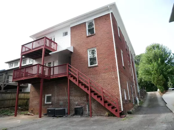 Back view of a red brick house with a red wooden staircase and deck leading to the second and third floors. Two outdoor HVAC units are placed at the base of the house.