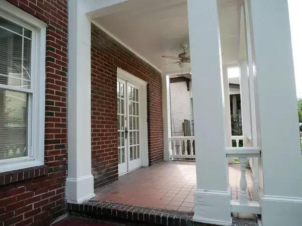 Covered front porch with white columns, red brick walls, tiled floor, and double French doors.