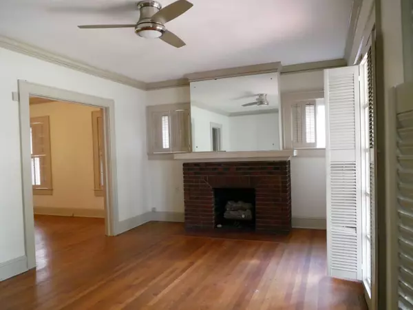 Living room with hardwood floors, ceiling fan, brick fireplace, and large mirror above mantel.