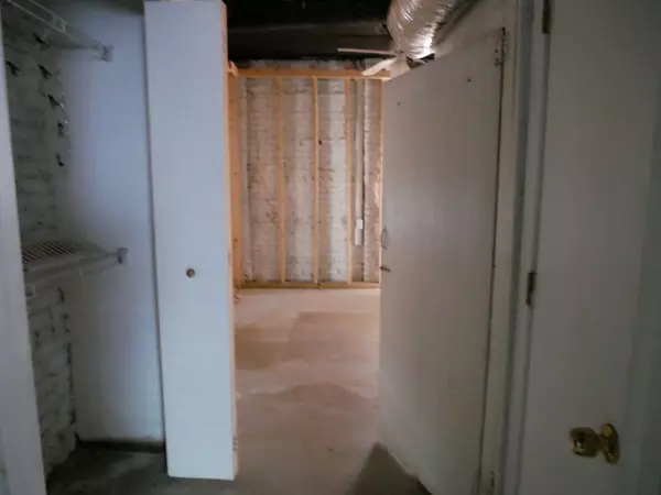 Basement entry with open closet space, white painted brick walls, exposed framing, and visible ductwork overhead.