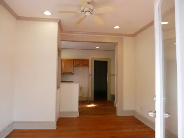 Interior room with hardwood floors, ceiling fan, and recessed lighting leading into kitchen with wooden cabinets.