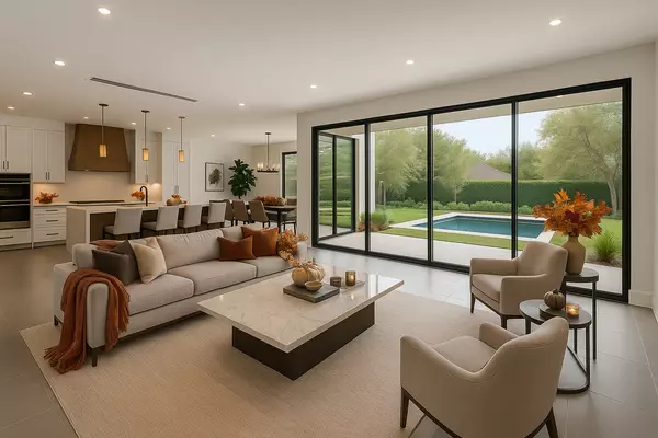 Open-concept living space in a luxury Bellaire home featuring a modern kitchen with wood-accent range hood, oversized island, and floor-to-ceiling glass doors overlooking a private backyard pool and lush landscaping