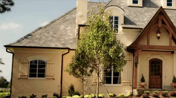 Front view of a luxury French-country style estate in Texas with manicured landscaping, arched windows, and detailed rooflines under a clear blue sky — representing high-end real estate appeal for discerning home sellers.