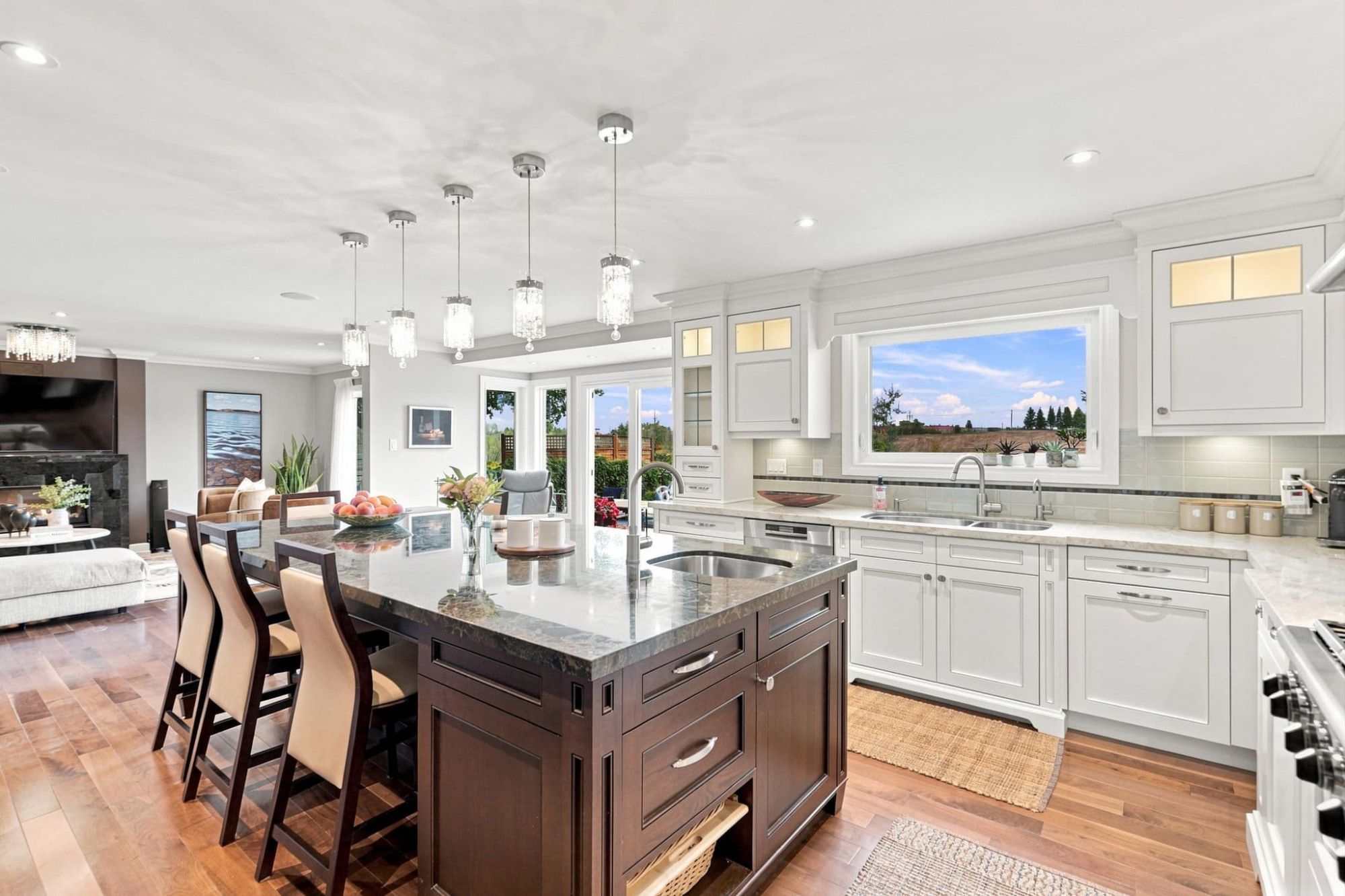 Bright kitchen with double stainless steel sink, white cabinetry, potted plants and window overlooking a backyard swimming pool