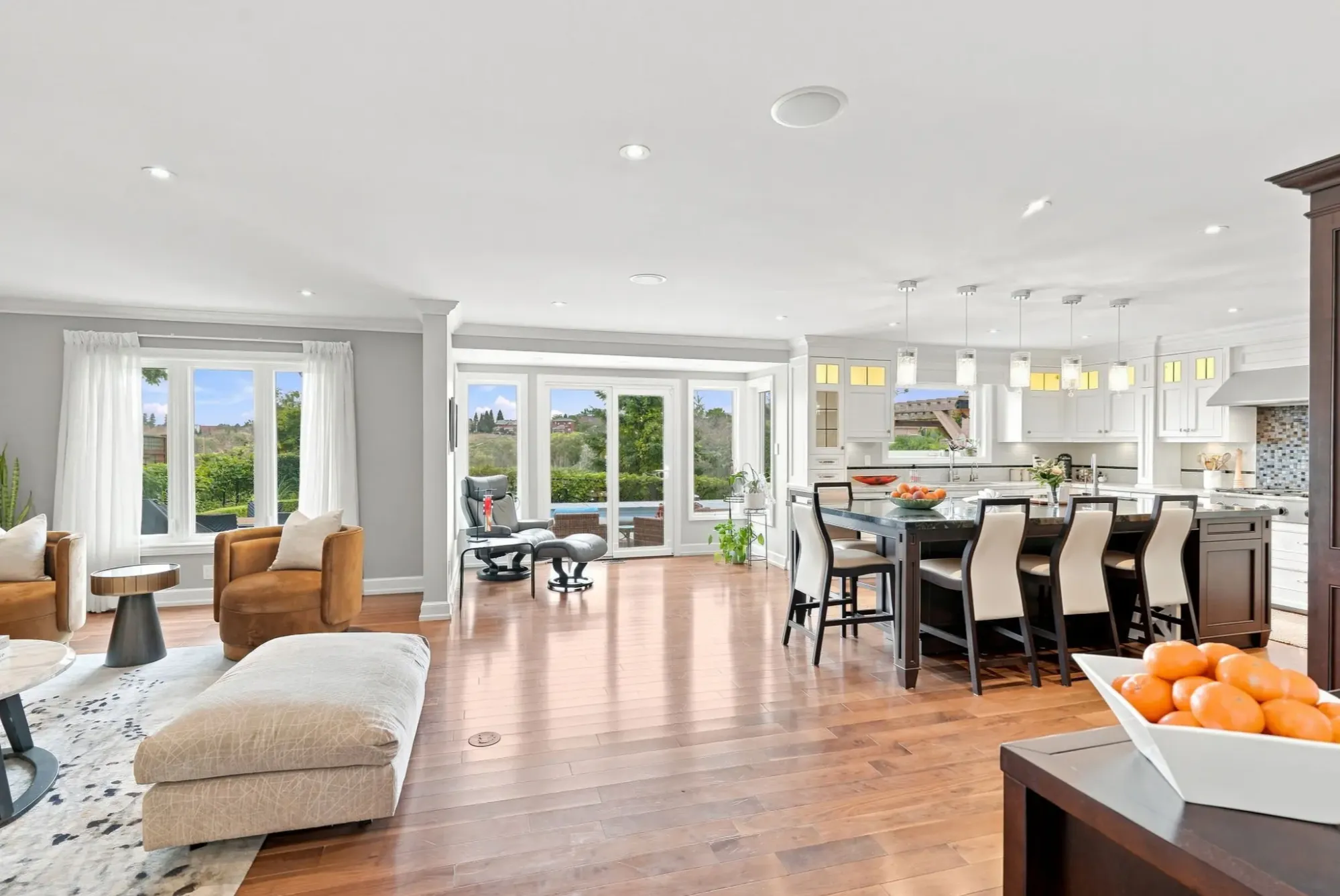 Bright open-concept living room connected to a spacious kitchen with a large island, wood floors and garden-facing windows.